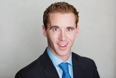 Young male criminal defense attorney wearing a blue suit and tie posing for a headshot photo